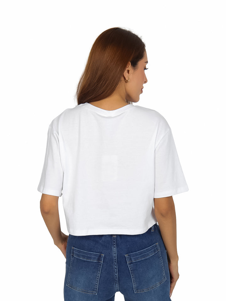 Mujer vistiendo playera corta blanca con estampado de rostro en blanco y negro y pantalones cargo azules.