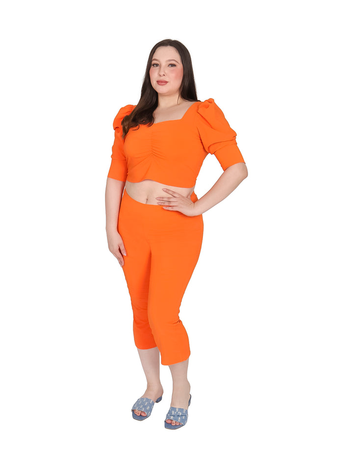 Mujer vistiendo un conjunto color naranja compuesto por blusa corta y pantalón capri.
