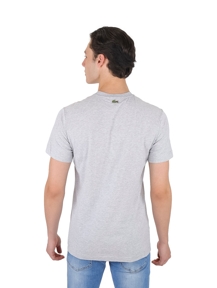 Hombre vistiendo una camiseta de manga corta color gris claro con logotipo de Lacoste en el pecho.