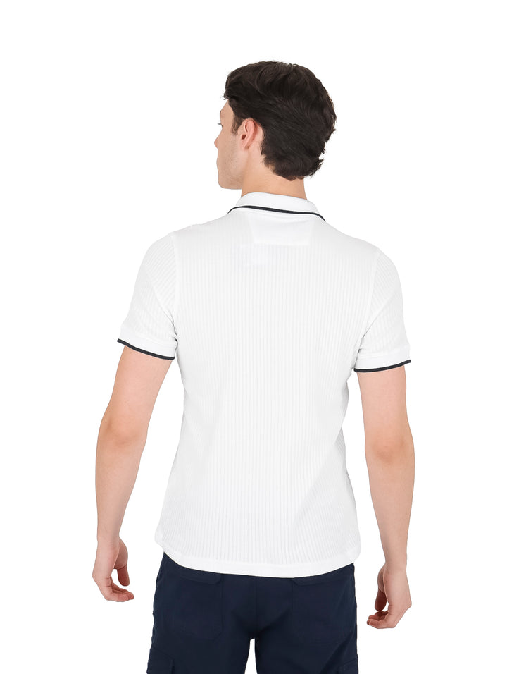 Playera polo blanca de manga corta con ribetes negros en el cuello y los bordes de las mangas.