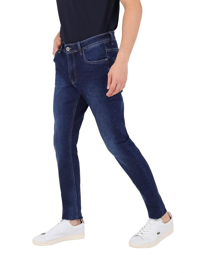 Hombre vistiendo pantalones jeans ajustados de color azul oscuro y tenis blancos.