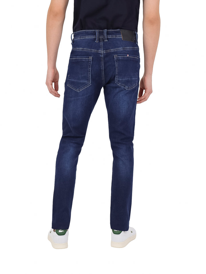 Hombre vistiendo pantalones jeans ajustados de color azul oscuro y tenis blancos.