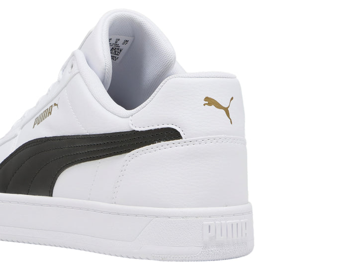 Tenis PUMA blancos con franja negra lateral y detalles dorados en la lengüeta.