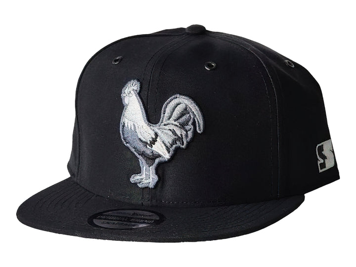 Gorra snapback color negro con un bordado frontal de un gallo blanco y gris.
