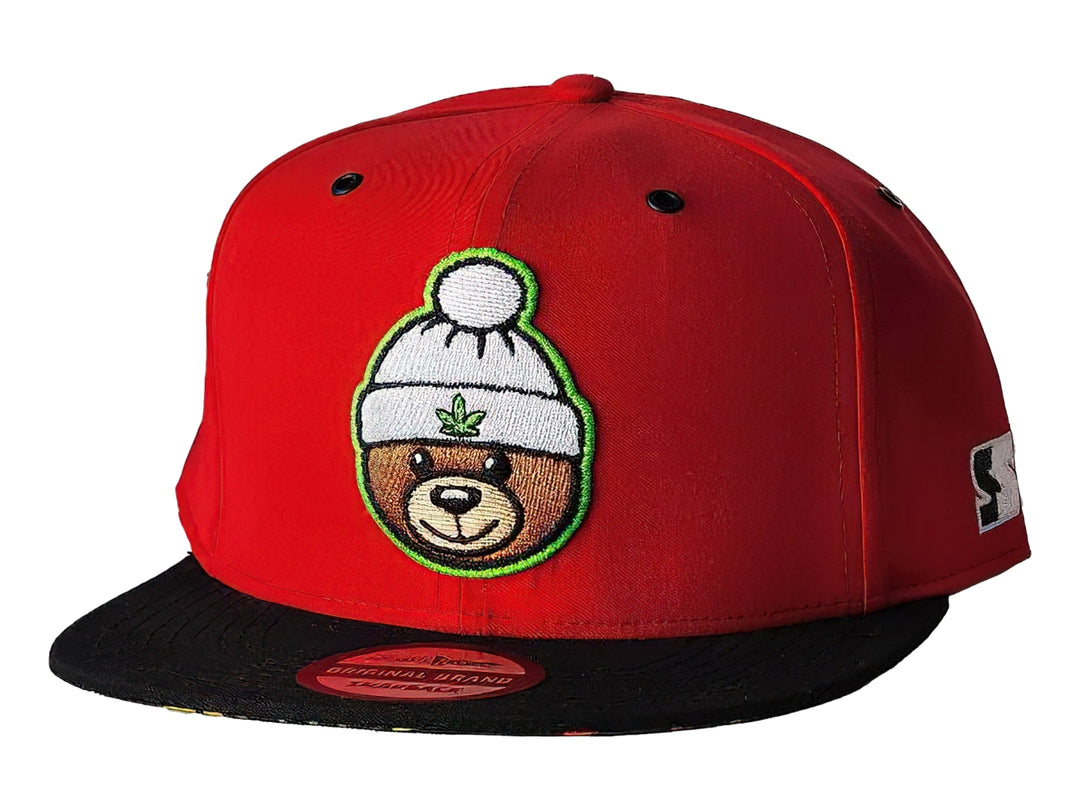 Gorra snapback roja con visera negra y un parche bordado de un oso con gorro blanco en el frente.