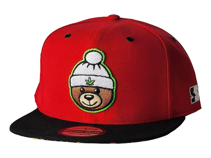 Gorra snapback roja con visera negra y un parche bordado de un oso con gorro blanco en el frente.