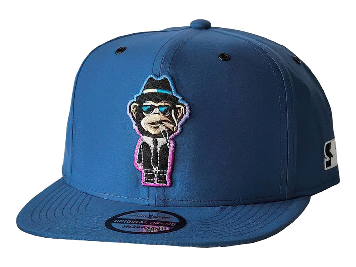 Gorra snapback color azul con un parche frontal bordado de un mono con traje y gafas de sol.