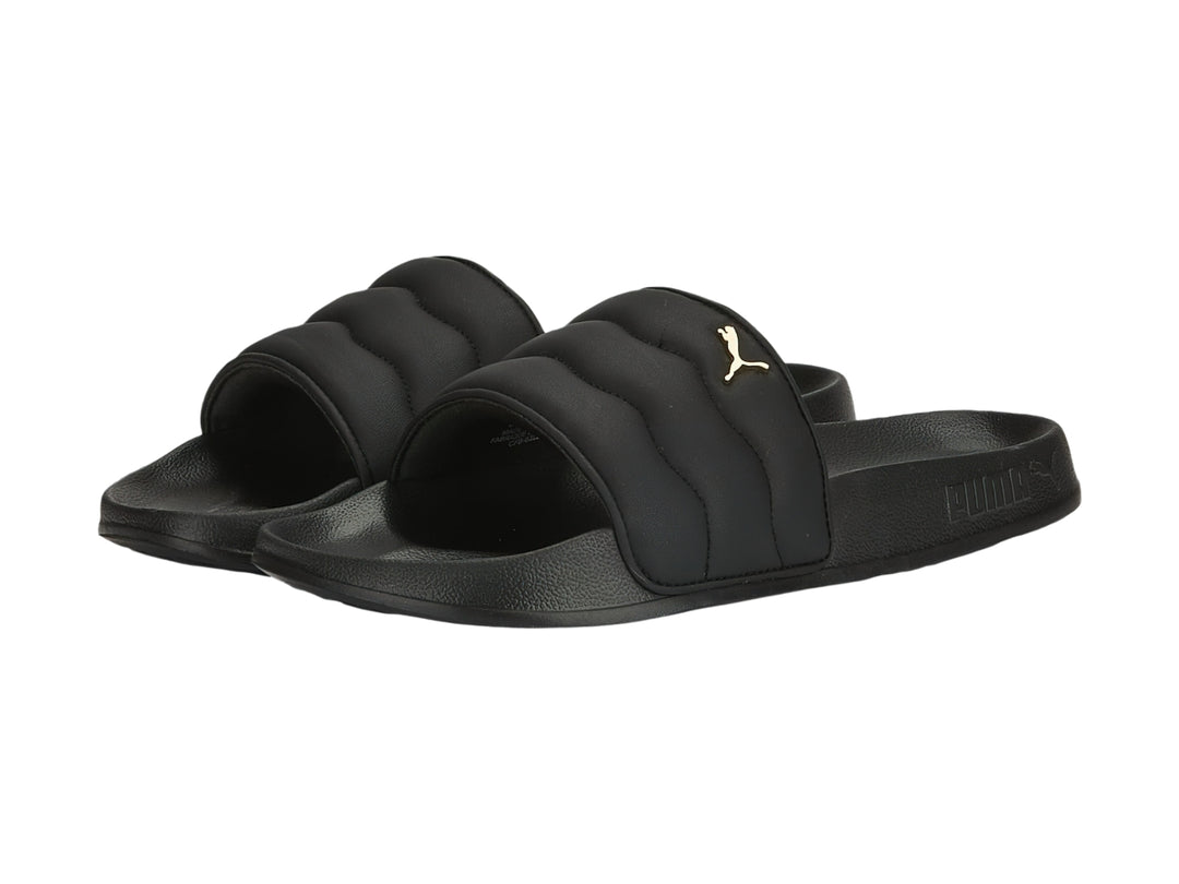 Sandalias PUMA negras con correa acolchada y logotipo dorado.