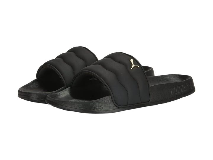 Sandalias PUMA negras con correa acolchada y logotipo dorado.