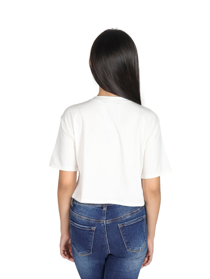Camiseta blanca crop top para niña con estampado artístico de un rostro y joyas coloridas.