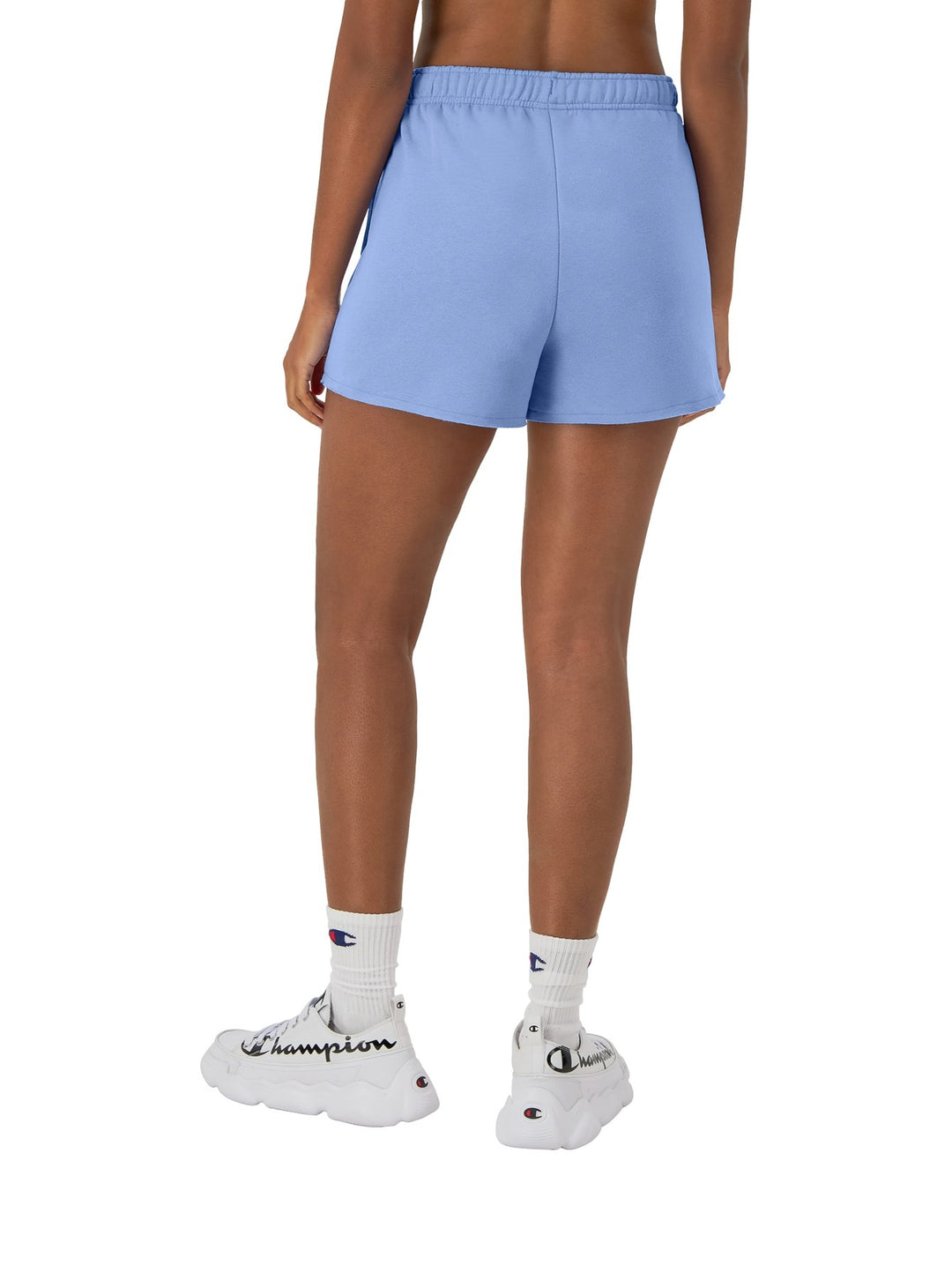 Mujer vistiendo shorts deportivos Champion en color azul plaster blue con tenis blancos.