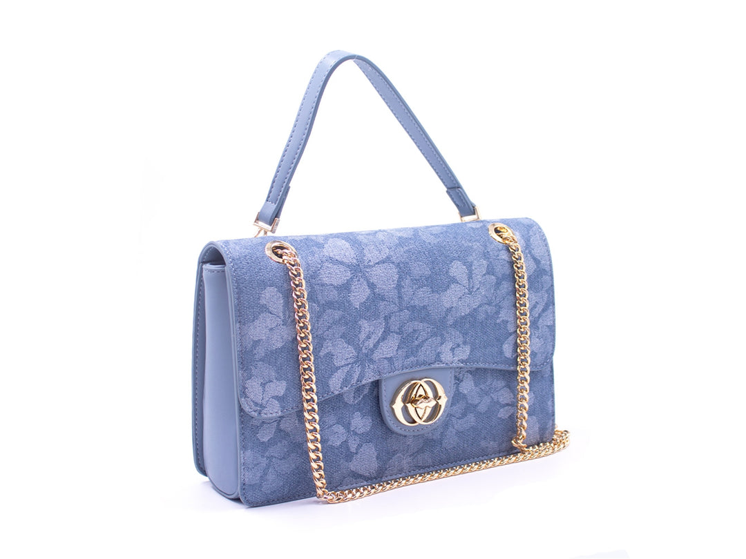 Bolso azul con estampado floral, asa corta y correa de cadena dorada con cierre metálico central.