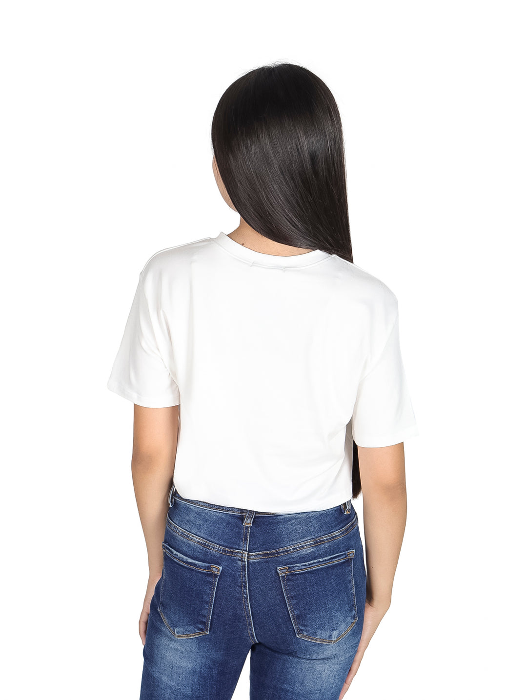 Niña vistiendo camiseta crop blanca con estampado colorido estilo años 70 y jeans azules.