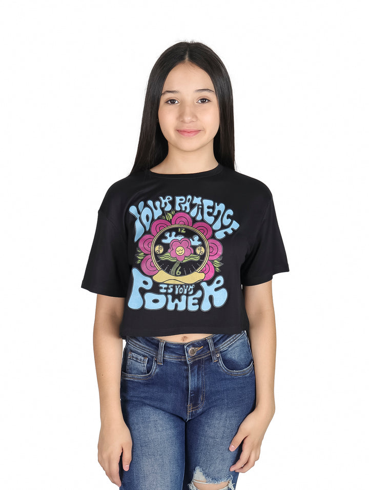 Niña vistiendo camiseta crop top negra con estampado colorido estilo años 70 y jeans azules.