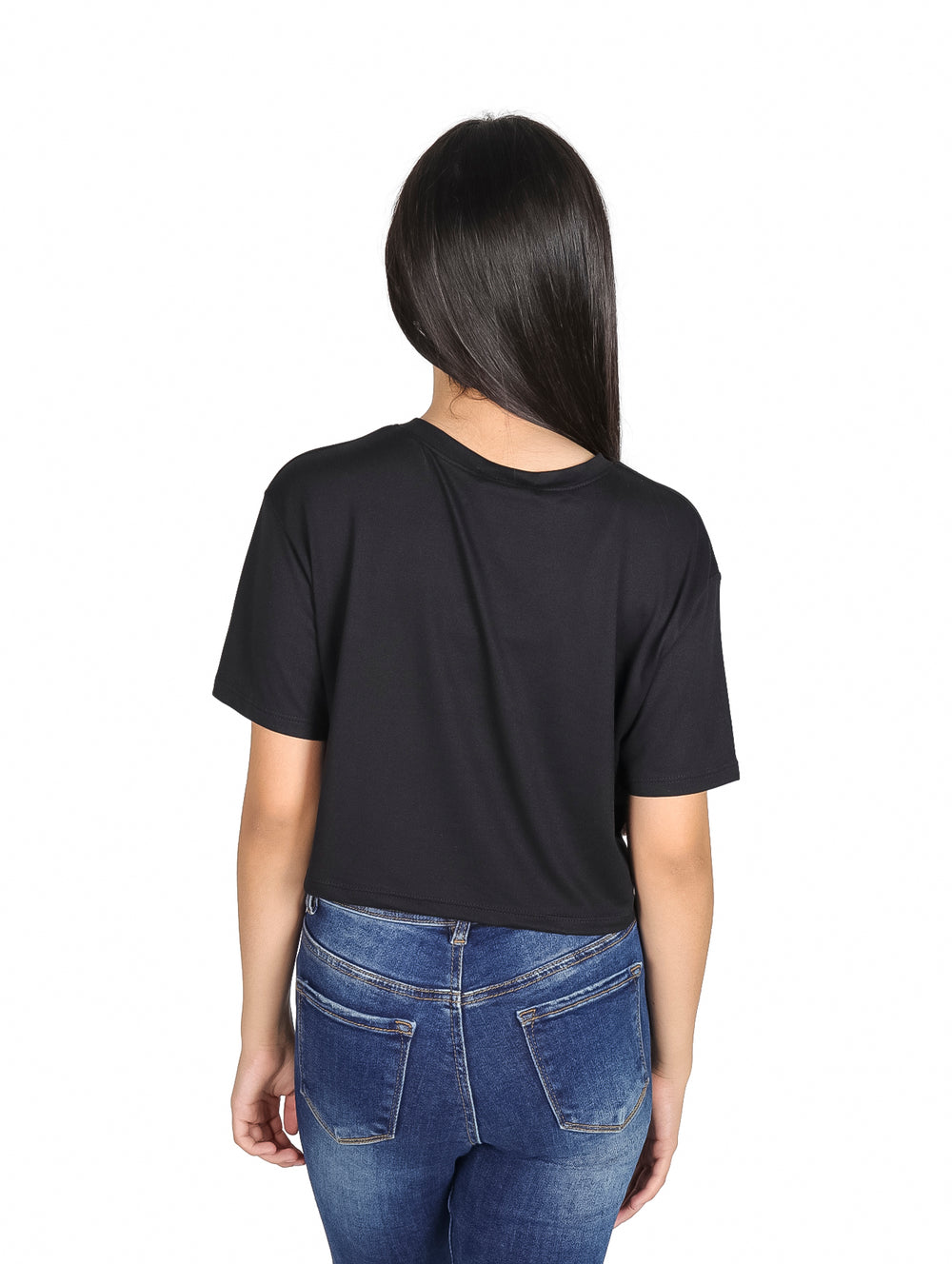 Niña vistiendo camiseta crop top negra con estampado colorido estilo años 70 y jeans azules.