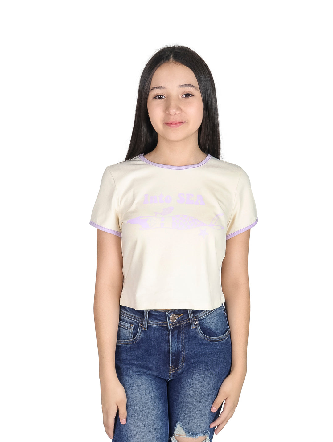 Niña vistiendo camiseta crop top color crema con detalles y estampado en morado y pantalones jeans azules.