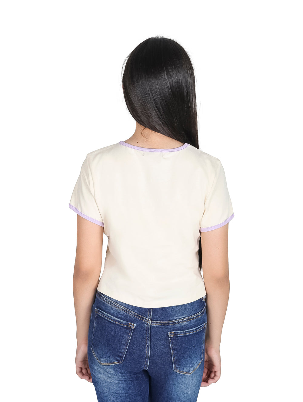 Niña vistiendo camiseta crop top color crema con detalles y estampado en morado y pantalones jeans azules.