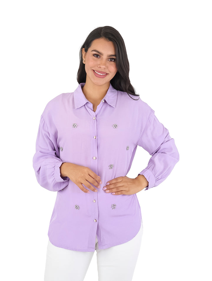 Mujer vistiendo camisa de color lila con manga larga y pequeños detalles decorativos brillantes en el frente.