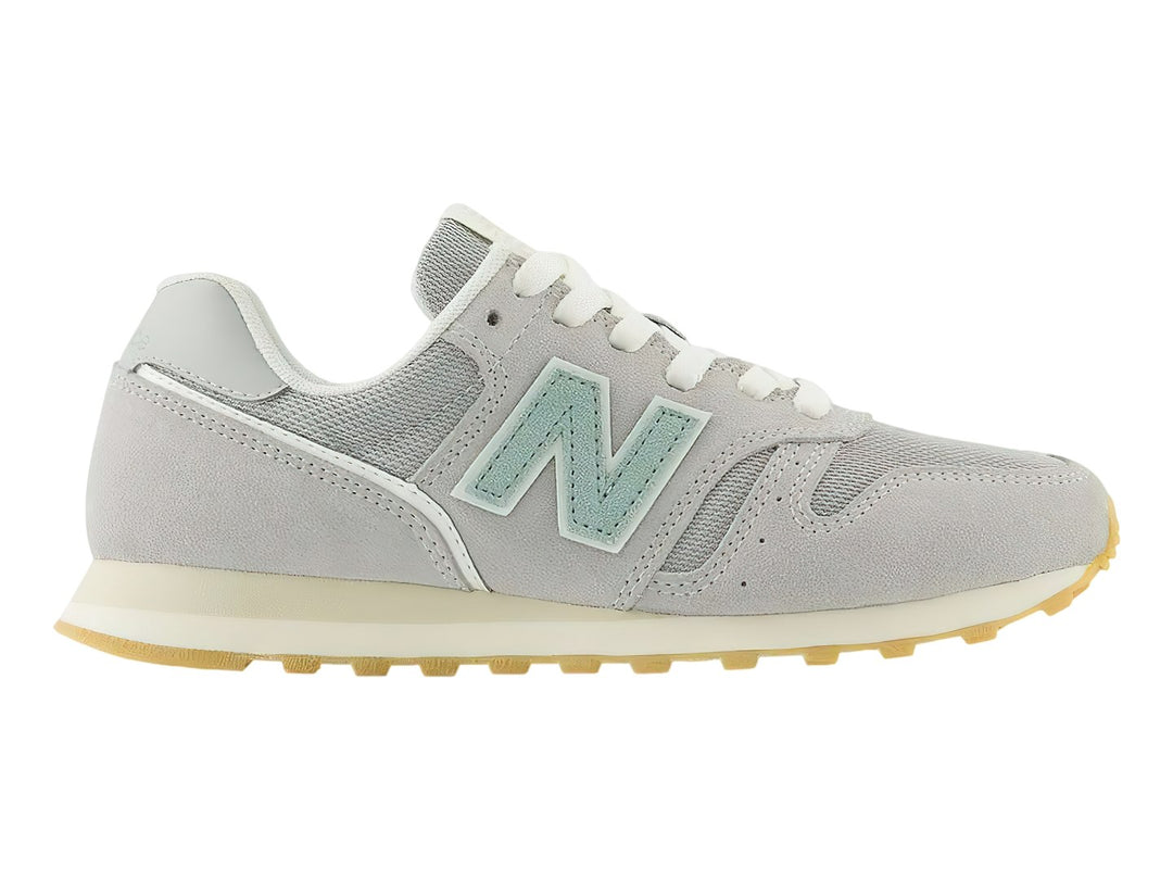 Tenis New Balance 373 color gris Raincloud con detalles en azul claro y suela color goma.