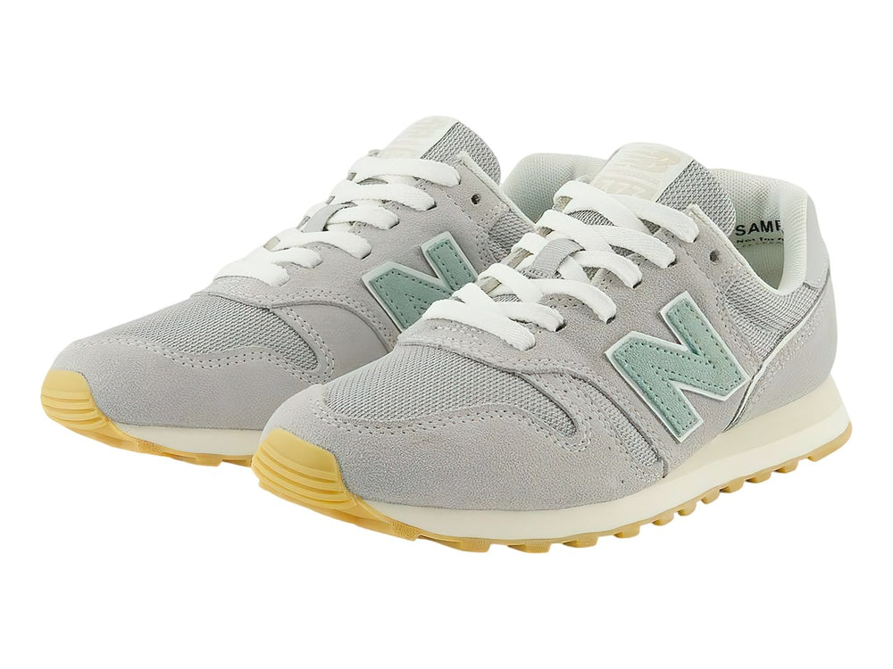 Tenis New Balance 373 color gris Raincloud con detalles en azul claro y suela color goma.