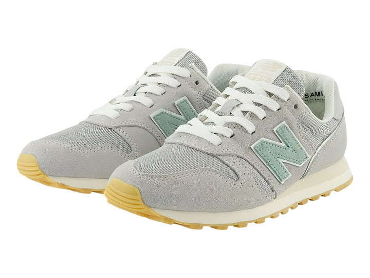 Tenis New Balance 373 color gris Raincloud con detalles en azul claro y suela color goma.