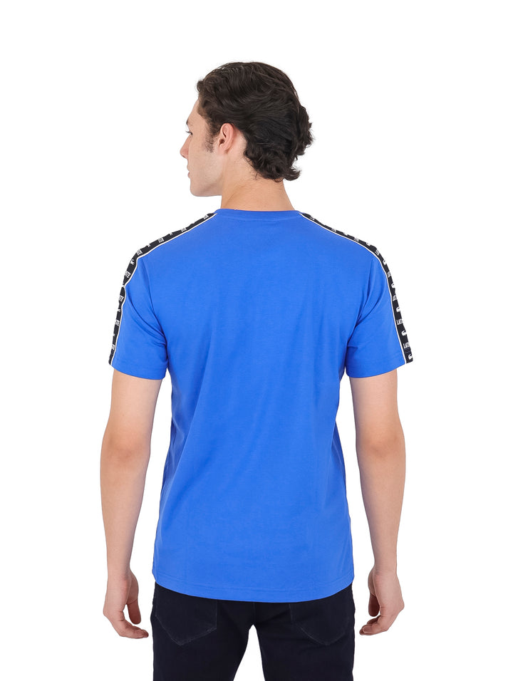 Hombre vistiendo camiseta azul de manga corta marca Lacoste con cintas decorativas negras en los costados.