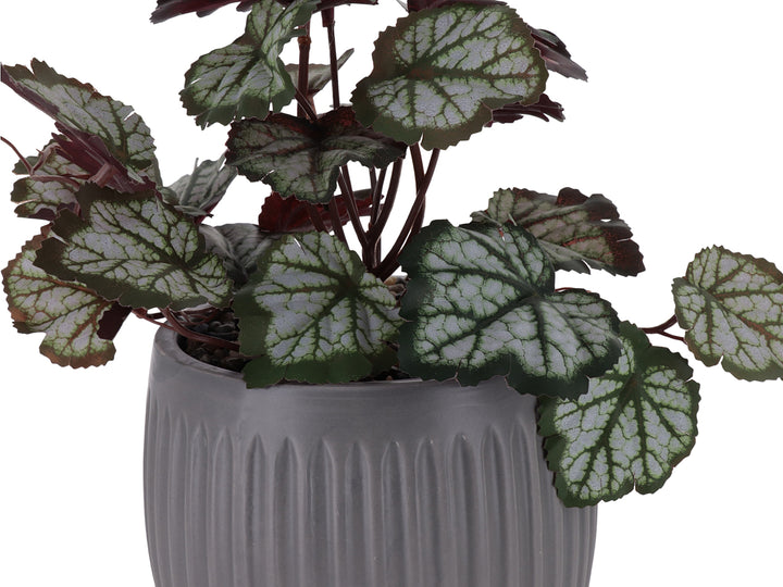 Planta artificial con hojas verdes y rojas en maceta de dolomita gris acanalada.