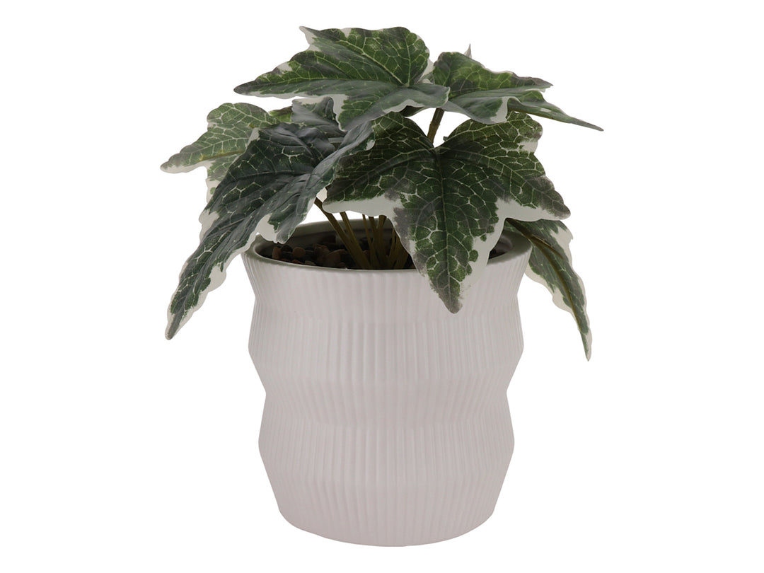 Planta artificial con hojas verdes en maceta de cerámica blanca con textura de rayas verticales.
