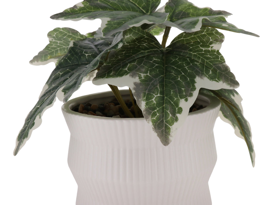 Planta artificial con hojas verdes en maceta de cerámica blanca con textura de rayas verticales.