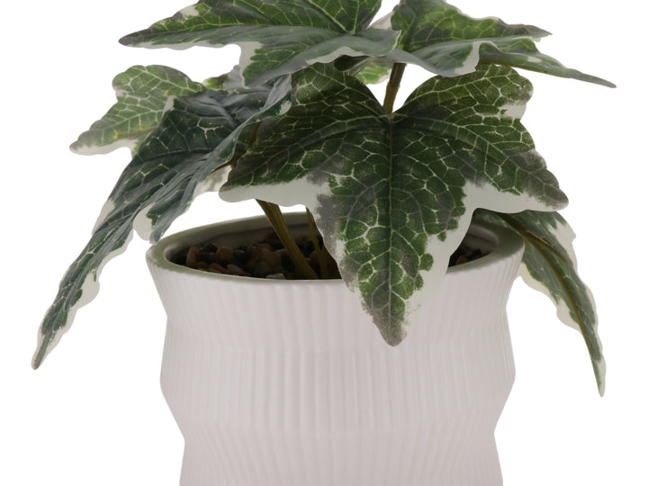 Planta artificial con hojas verdes en maceta de cerámica blanca con textura de rayas verticales.