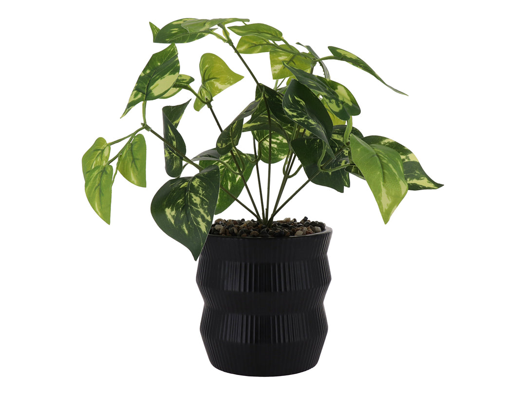 Planta artificial con hojas verdes en maceta decorativa de color negro con textura de rayas verticales.