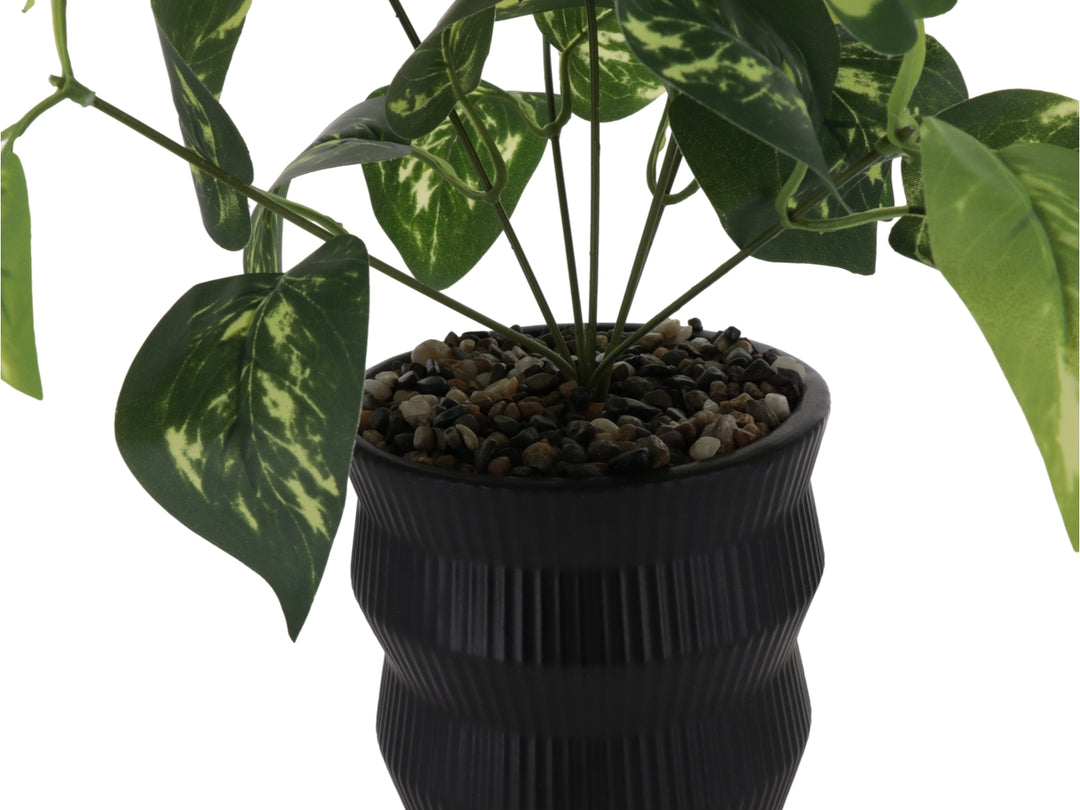 Planta artificial con hojas verdes en maceta decorativa de color negro con textura de rayas verticales.