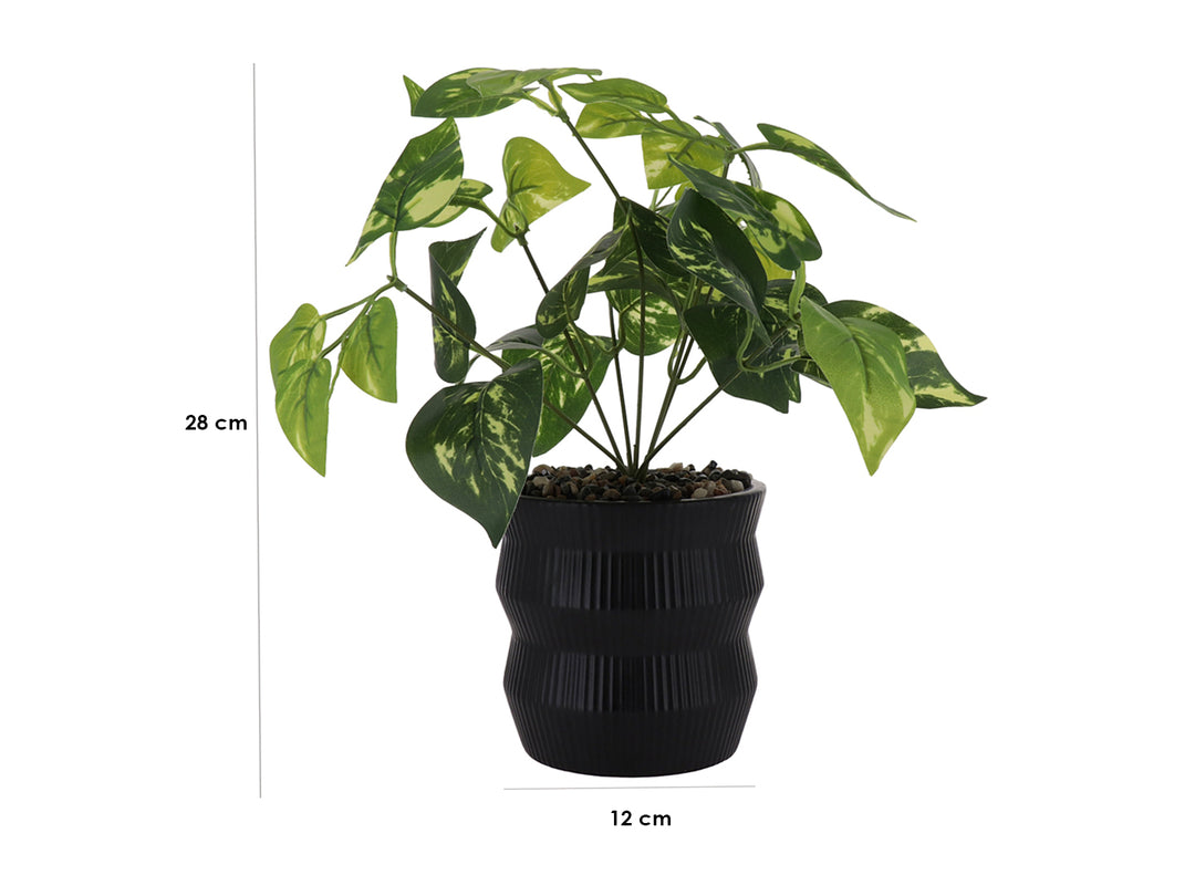 Planta artificial con hojas verdes en maceta decorativa de color negro con textura de rayas verticales.