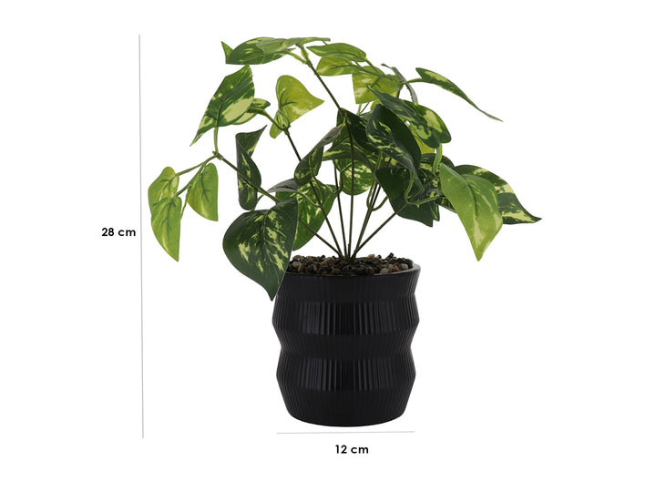 Planta artificial con hojas verdes en maceta decorativa de color negro con textura de rayas verticales.