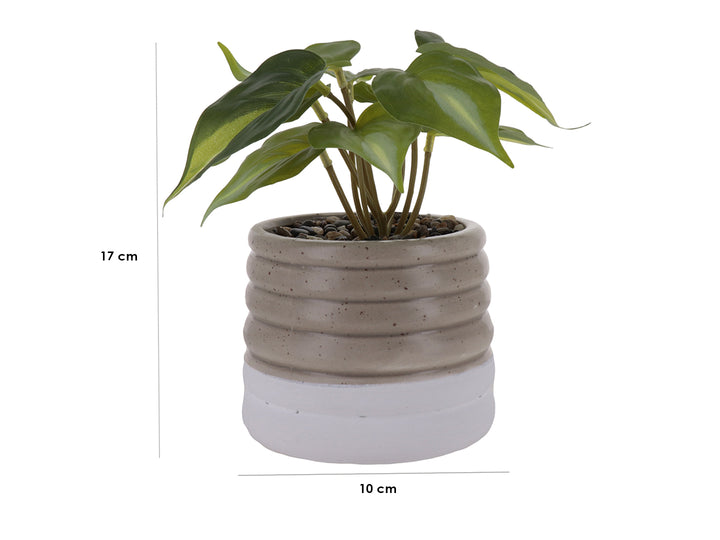 Planta artificial verde en maceta decorativa de cerámica color beige con diseño ondulado y base blanca.
