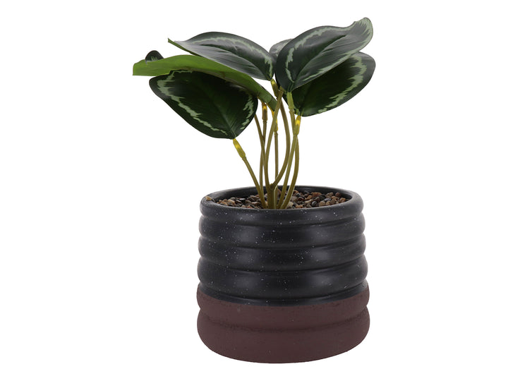 Planta artificial con hojas verdes en maceta de cerámica negra con diseño ondulado y base marrón.