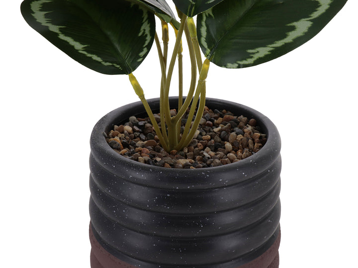 Planta artificial con hojas verdes en maceta de cerámica negra con diseño ondulado y base marrón.