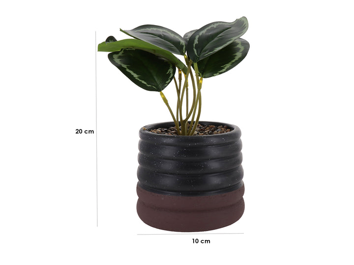 Planta artificial con hojas verdes en maceta de cerámica negra con diseño ondulado y base marrón.