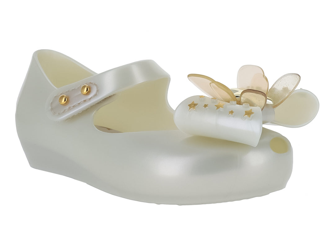 Zapato blanco brillante para niña de Mini Melissa con correa y adorno de moño con estrellas doradas.