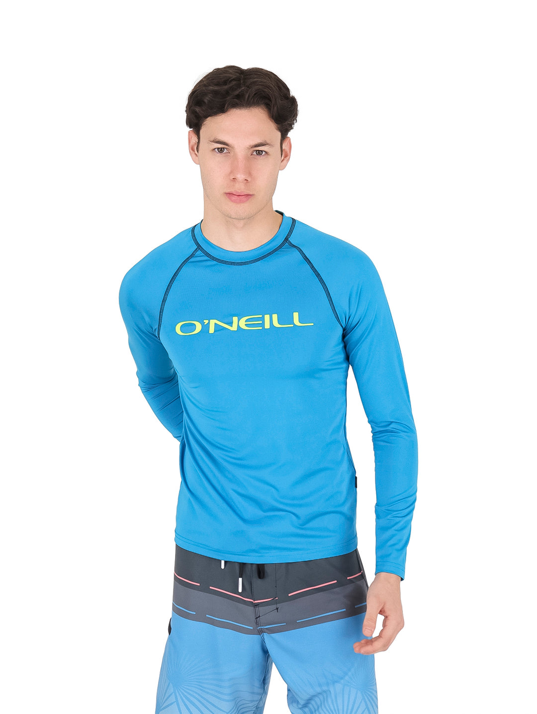 Hombre vistiendo playera rashguard azul de manga larga marca O'Neill y shorts azules.