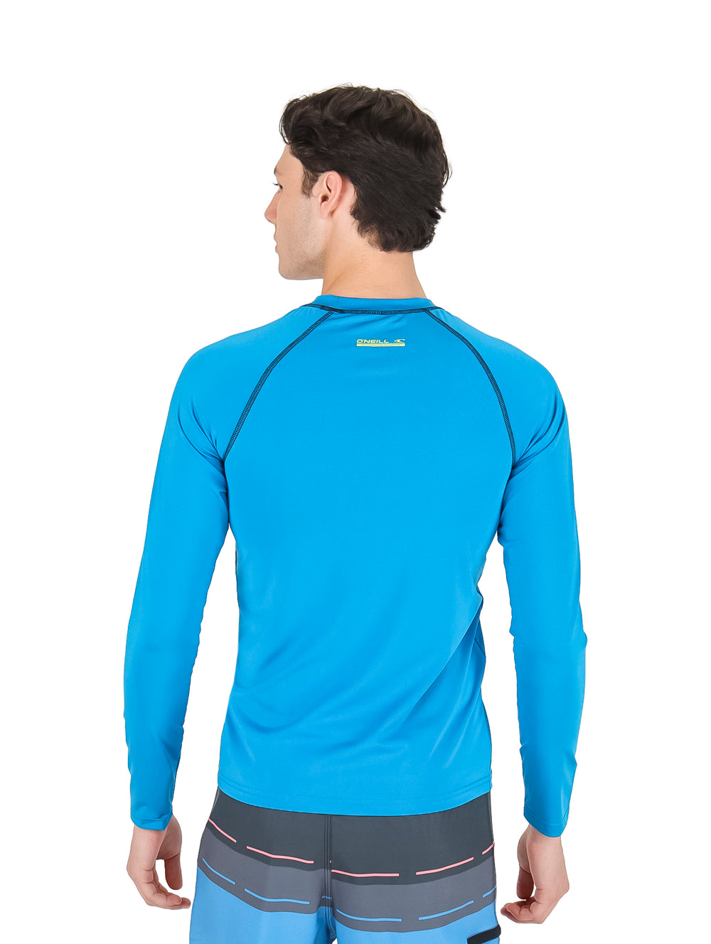 Hombre vistiendo playera rashguard azul de manga larga marca O'Neill y shorts azules.