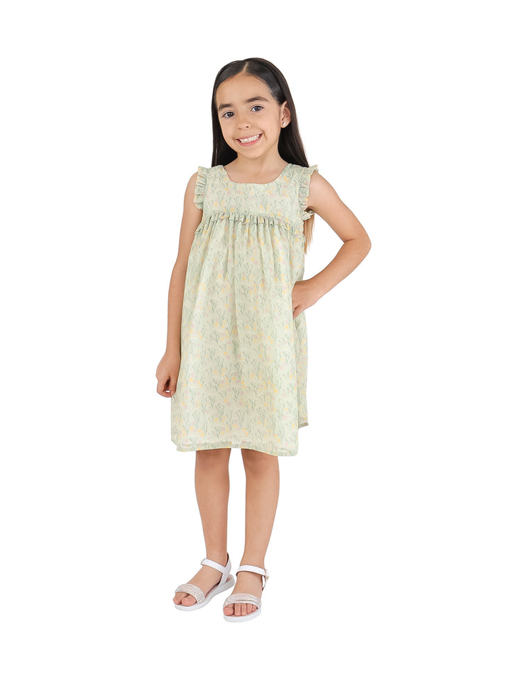 Niña vistiendo un vestido corto color verde agua con estampado floral amarillo y sandalias blancas.