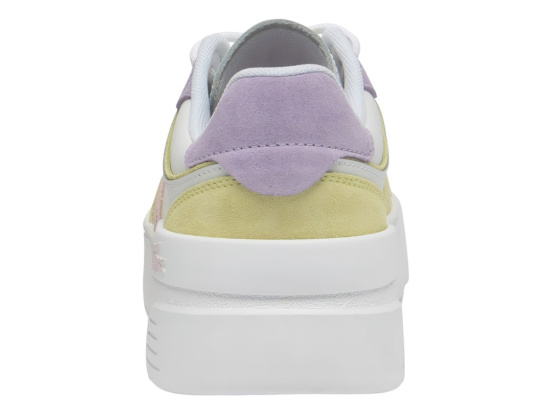 Tenis Lacoste blancos con detalles en morado y amarillo y suela de plataforma blanca.
