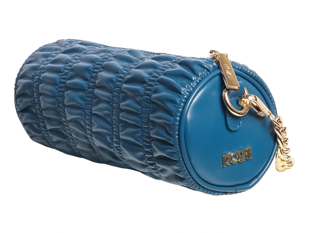 Bolsa cilíndrica azul con textura fruncida y detalles metálicos dorados de la marca ROZE.