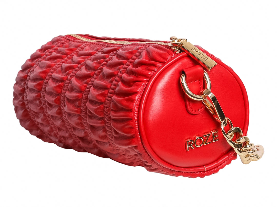 Bolso pequeño cilíndrico de color rojo con textura fruncida y detalles metálicos en dorado de la marca ROZE.