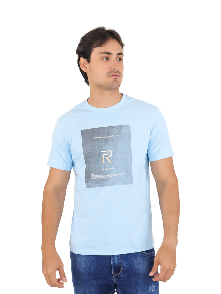 Hombre vistiendo playera azul claro de manga corta con estampado gráfico frontal y pantalones jeans azules.