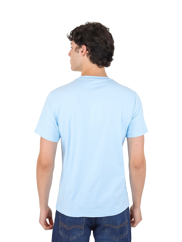 Hombre vistiendo una playera azul claro de manga corta con un pequeño logo en el pecho.