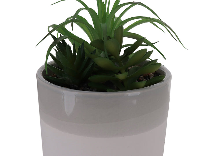 Planta artificial verde en maceta cilíndrica de cerámica bicolor blanco y beige con acabado brillante.