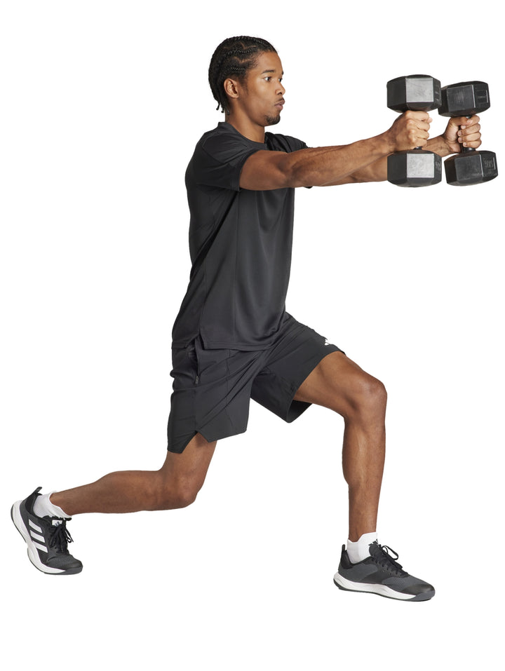 Hombre realizando ejercicio con mancuernas vistiendo shorts deportivos negros de Adidas.