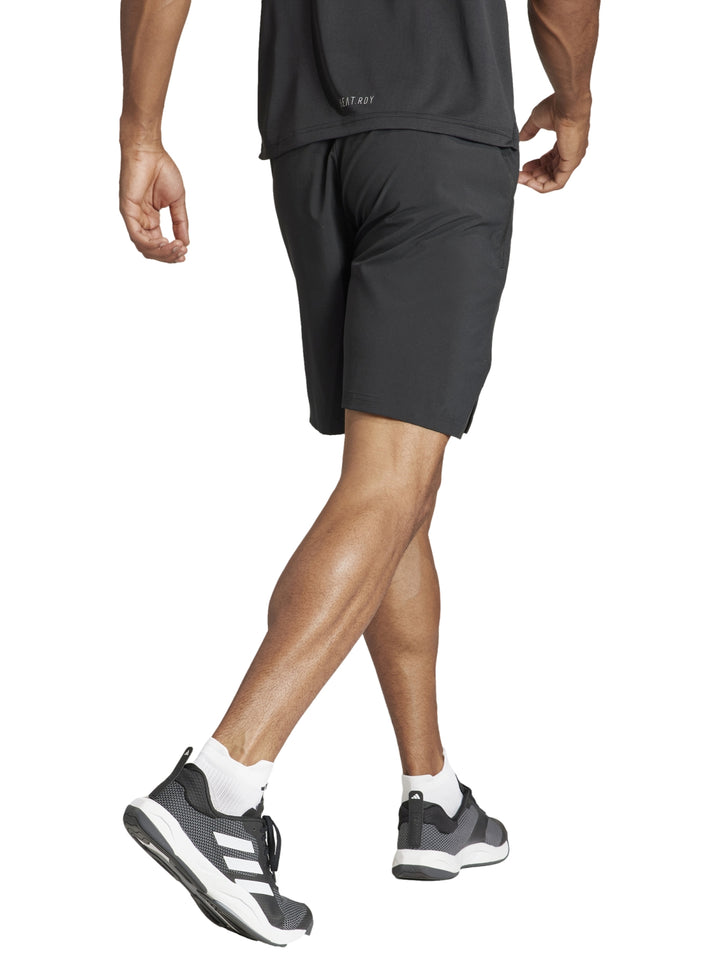 Hombre realizando ejercicio con mancuernas vistiendo shorts deportivos negros de Adidas.